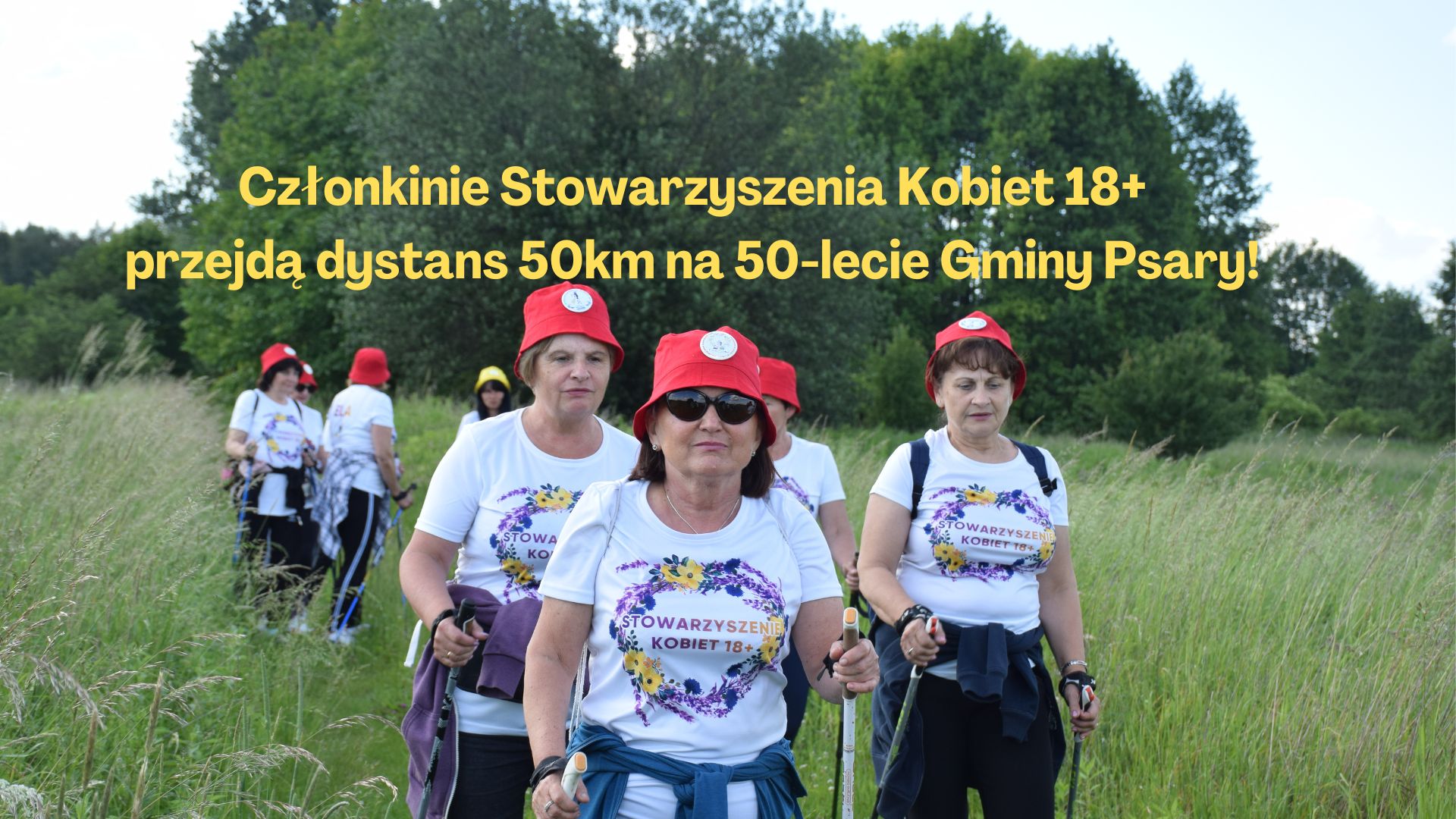 Na zdjęciu znajdują się członkinie ze Stowarzyszenia Kobiet 18+, które uprawiają nordic walking. Panie ubrane są w czerwone czapki i białe koszulki z kolorowym wzorem. Na środku znajduje się żółty napis: Członkinie Stowarzyszenia Kobiet 18+ przejdą dystans 50 km na 50-lecie Gminy Psary!