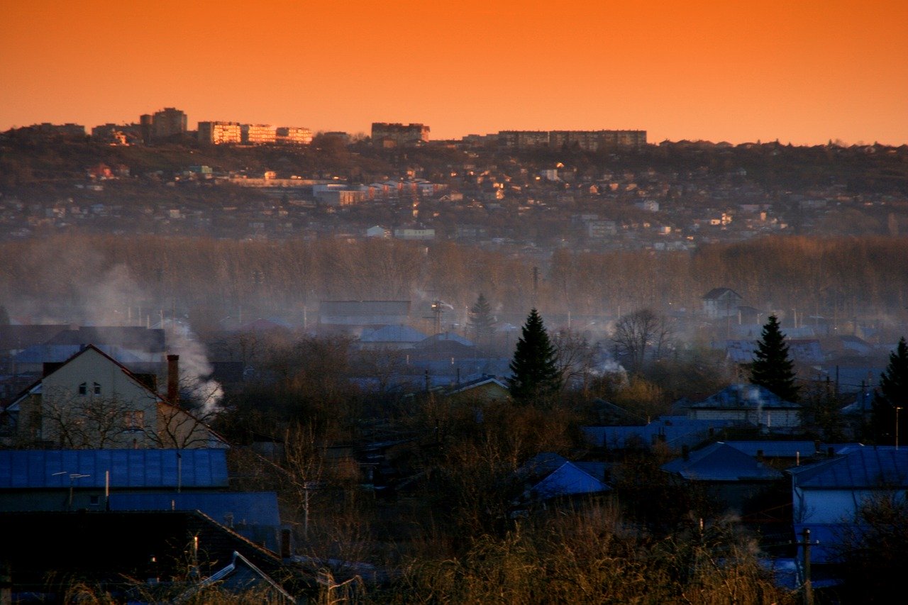 Grafika przedstawia miasto o zachodzie słońca, pokryte smogiem 