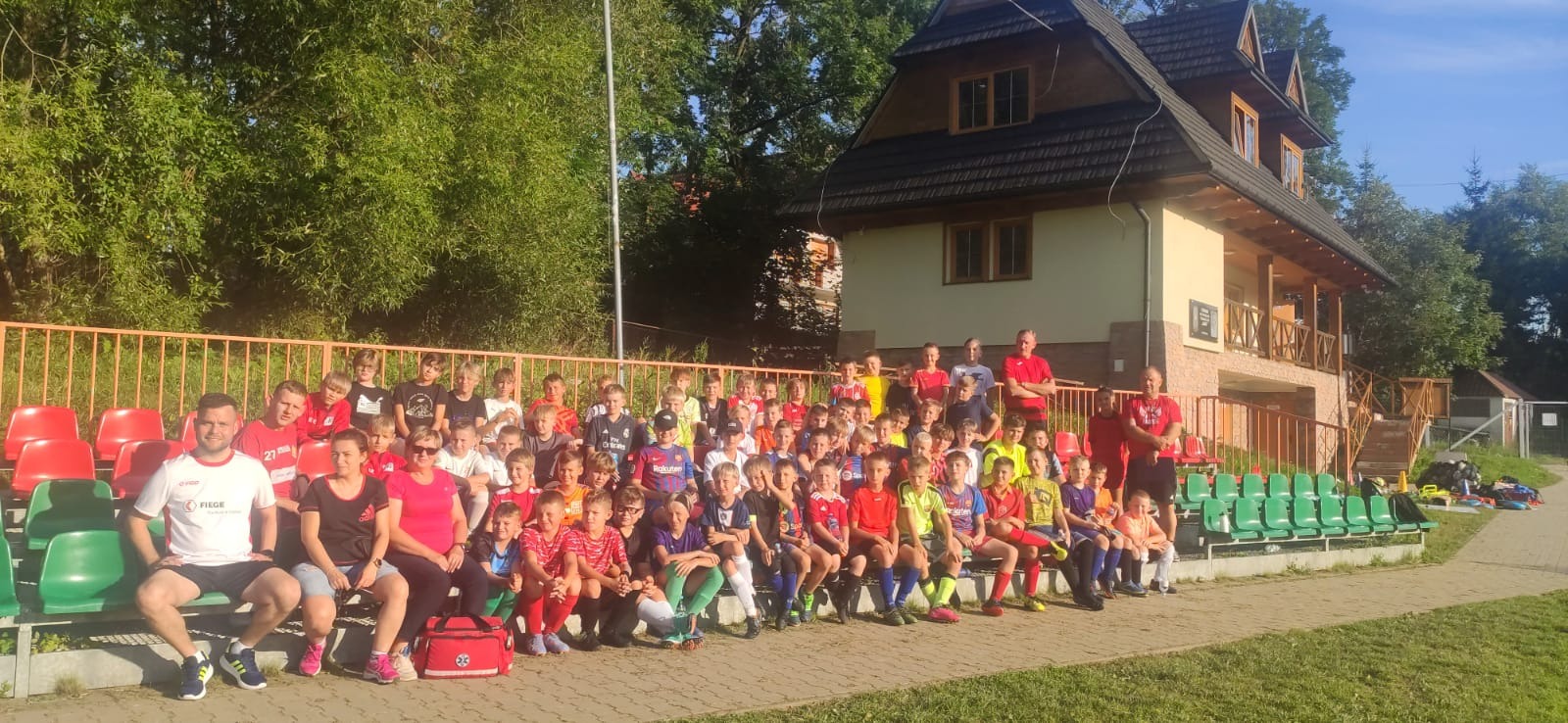 Fotografia przedstawia zawodników Akademii Piłki Nożnej podczas obozu w Białym Dunajcu.Zawodnicy wraz z trenerami siedzą na trybunach.