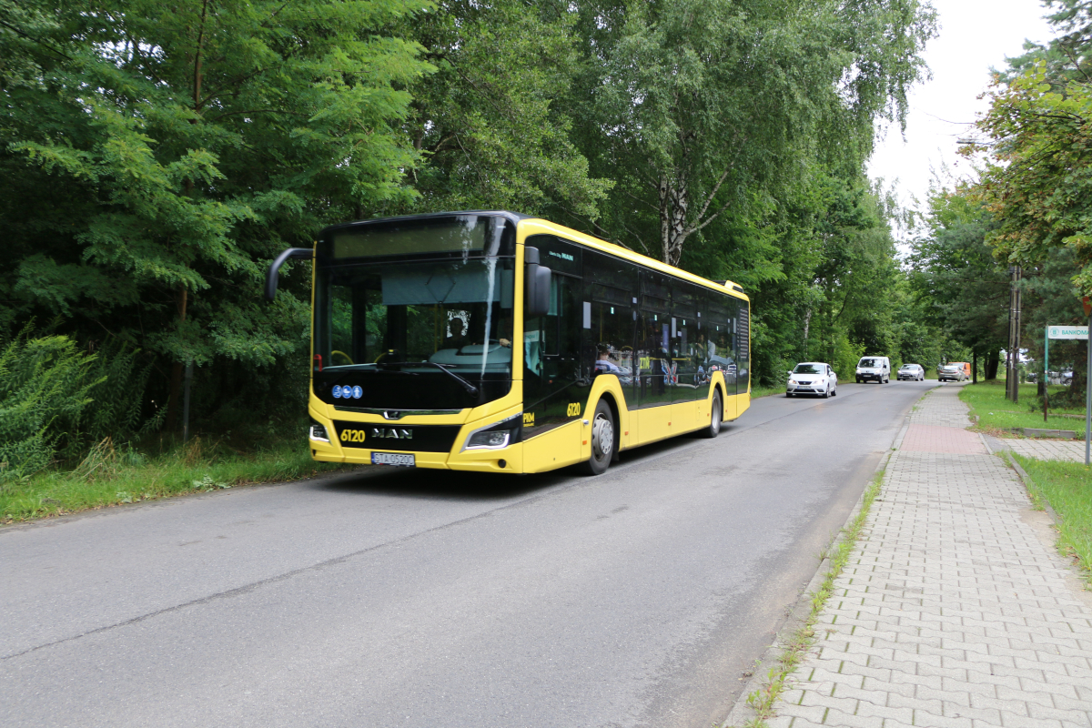 Zdjęcie przedstawia jadący żółto-czarny autobus, za nim jadą samochody