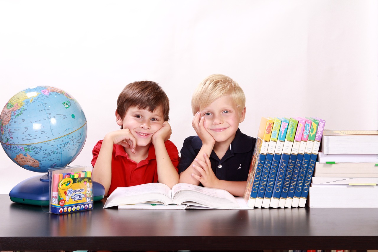 Zdjęcie przedszkwia dwóch chłopców, po lewej stronie znajduje się globus, po prawej książki
