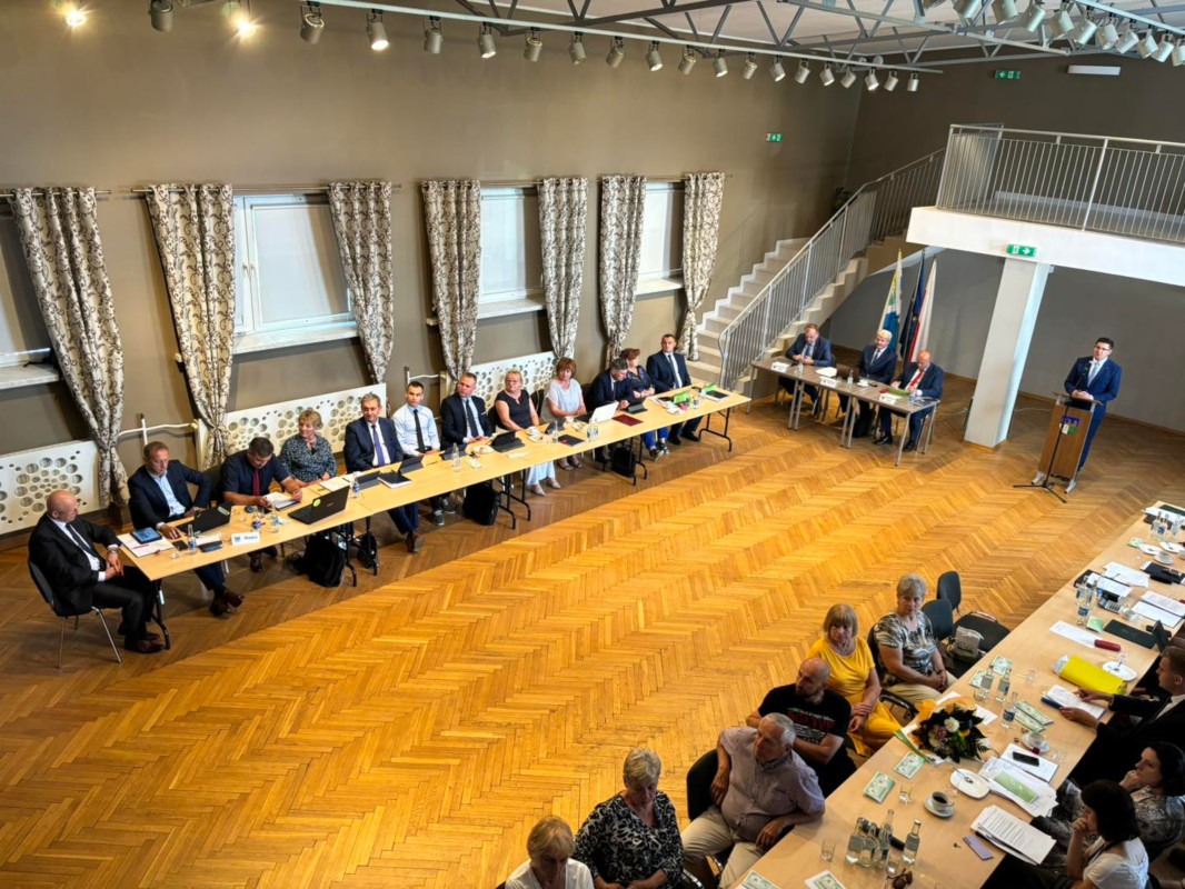 Zdjęcie robione z góry przedstawia radnych siedzących przy stole w sali bankietowej